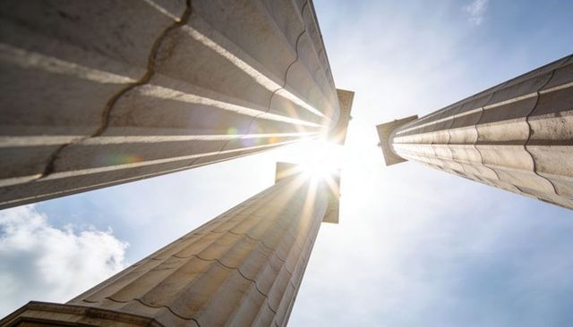 Sunburst through fluted columns converging toward sky - monumental neoclassical colonnade
