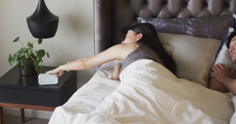 Woman reaching for alarm clock in bed cozy morning routine with partner