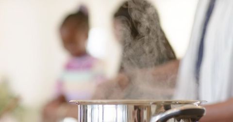 Diverse family watching steam rising from stainless steel pot on stovetop in warm kitchen