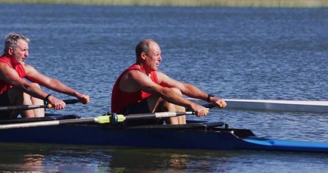 Mature men powering blue racing shell on calm lake during outdoor rowing training for teamwork