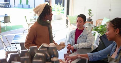 Diverse customers ordering coffee at modern café counter with female barista assisting