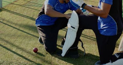 Diverse teammates adjusting cricket batting pads and gloves during focused practice session