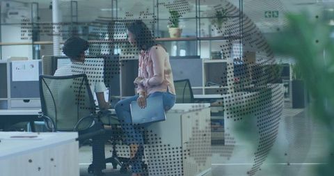 Colleagues discussing laptop in open-plan office with dotted glass partition