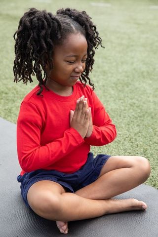 Young Child Meditating Outdoors on Exercise Mat in Open Land