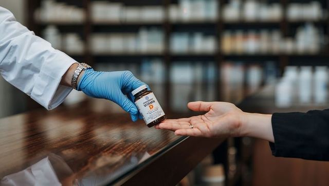 Pharmacist handing vitamin d bottle to customer over counter with gloved clinical care