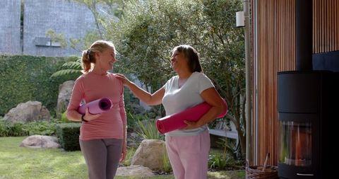 Smiling Female Friends Holding Yoga Mats in Garden with Stove