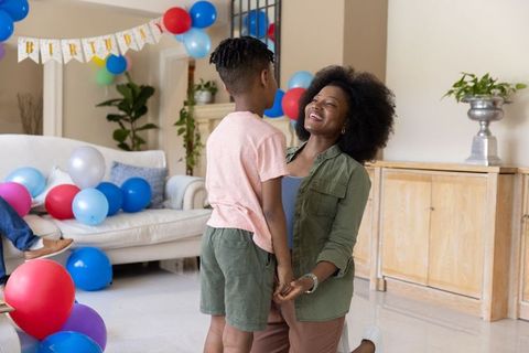 African american mother kneeling holding hands with son in colorful birthday celebration