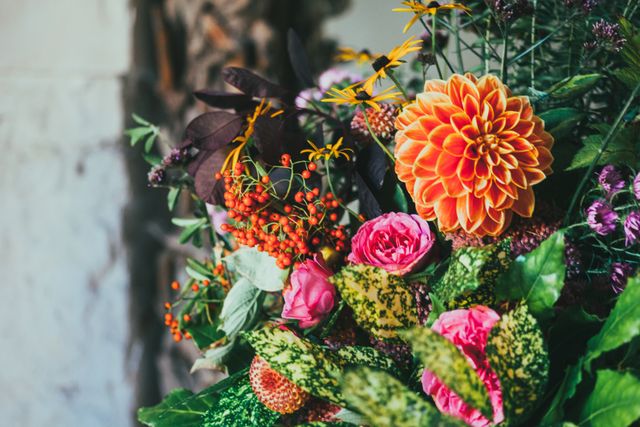 This image showcases a vibrant floral arrangement featuring bright dahlias, colorful roses, and various other garden flowers with lush green foliage. Ideal for use in home decor articles, gardening blogs, floral arrangement tutorials, and lifestyle magazines. It beautifully captures the essence of natural beauty and elegance.