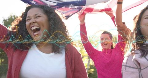Friends celebrating holding American flag outdoors laughing and waving in sunlit park