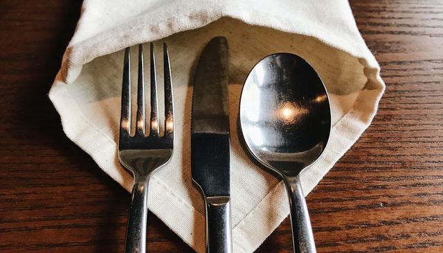 Stainless steel fork knife spoon resting in linen napkin pocket on rustic wooden table