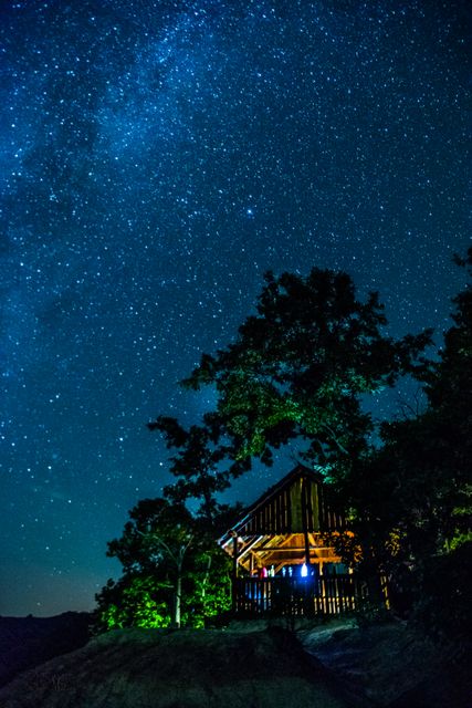 Rustic cabin nestled in a remote forest under a starry night sky with bright stars and clear view. Ideal for content focusing on nature retreats, outdoor adventures, escapism, solitude, peacefulness, and rustic living. Useful for travel blogs, book covers, nighttime photography collections, or meditation content.