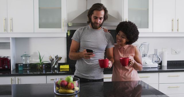 Couple enjoying their morning coffee together in a modern kitchen. They are casually dressed, engaged with a smartphone, and smiling, creating a warm, intimate atmosphere. Suitable for ads, blogs, or articles related to lifestyle, home, relationships, morning routines, or kitchen designs.