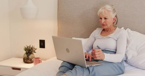 Senior Woman Working on Laptop in Bedroom with Minimalist Decor