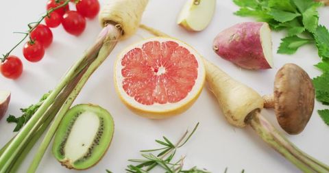 Displaying halved pink grapefruit and kiwi with cherry tomatoes and herbs flatlay