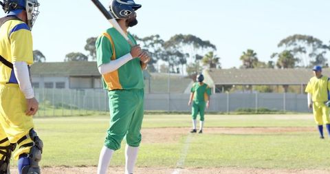 Batter Waiting at Home Plate with Catcher and Teammates on Sunny Baseball Field
