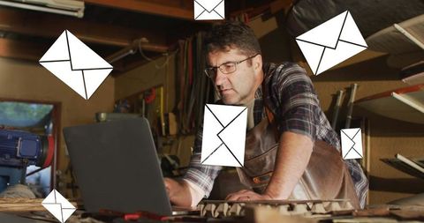 Carpenter using laptop surrounded by digital envelope icons