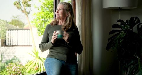 Peaceful Senior Woman Relaxing by Window with Warm Drink