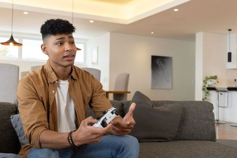 African american teen playing video games on couch gesturing gamer in modern living room