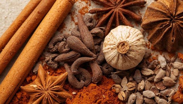 Warm assortment of whole and ground spices featuring cinnamon sticks, star anise, cardamom
