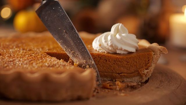 Slicing pumpkin pie with whipped cream on rustic wooden board, cozy autumn dessert