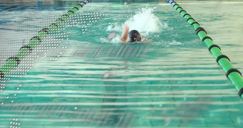 Swimmer swimming laps indoor pool wearing black cap and goggles with green lane lines