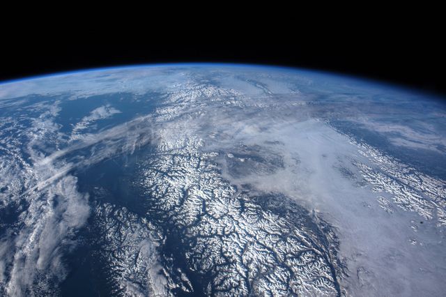 High-altitude view of Earth showcasing snow-covered mountain ranges alongside oceans. The curvature and thin atmosphere are visible, providing a breathtaking perspective from space. Perfect for use in educational materials, environmental campaigns, science presentations, and background images highlighting the beauty of our planet.