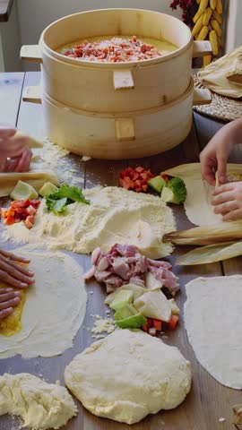 Vertical video flattening masa, layering fillings and wrapping tamales next to bamboo steamer
