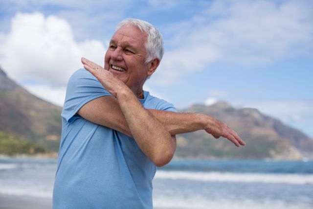 Happy senior man doing stretching exercise on the beach
