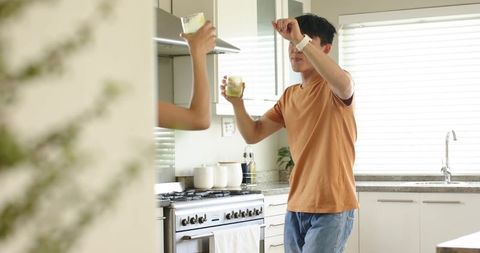 Couple toasting with green smoothies in bright modern kitchen, playful morning moment