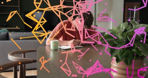 Writing at home leaning over journal with coffee mug, plant and neon geometric overlay