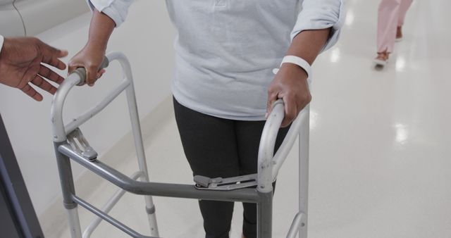 Woman using walker during recovery process in hospital corridor. Suitable for topics like patient rehabilitation, healthcare services, physical therapy, life in hospital, mobility aid.
