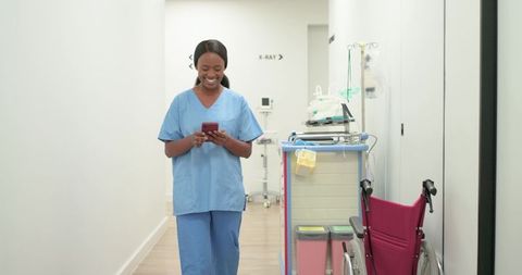 Smiling african american nurse walking hospital corridor using smartphone