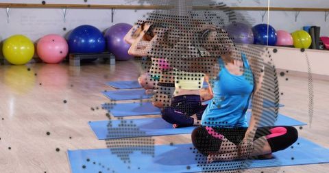 Group yoga stretching class on blue mats in bright fitness studio with exercise balls