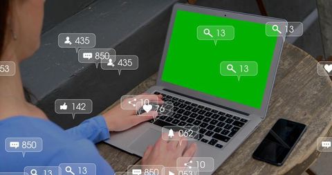 Man typing on laptop with green screen and floating social media notification overlays