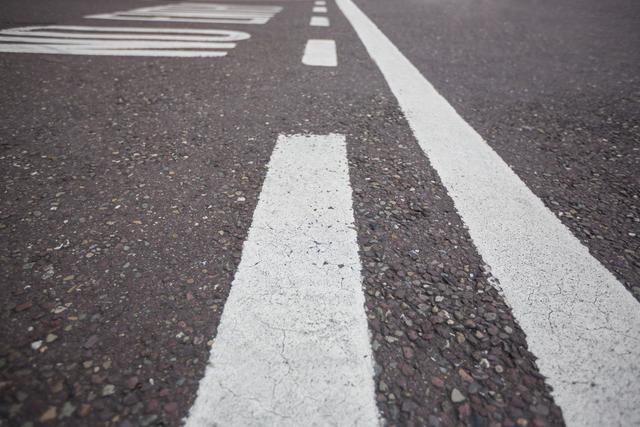 Close-up of road markings on an asphalt surface showing white lines and texture. Useful for illustrating urban infrastructure, transportation themes, or road safety concepts. Ideal for blogs, educational materials, travel websites, and urban planning presentations.