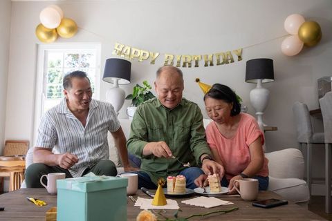 Asian family celebrating senior father's birthday at home with cake, balloons and gifts