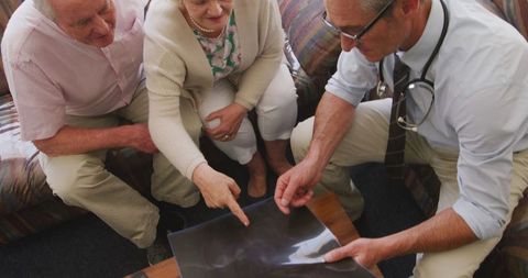 Senior couple consults doctor reviewing x-ray results in home setting