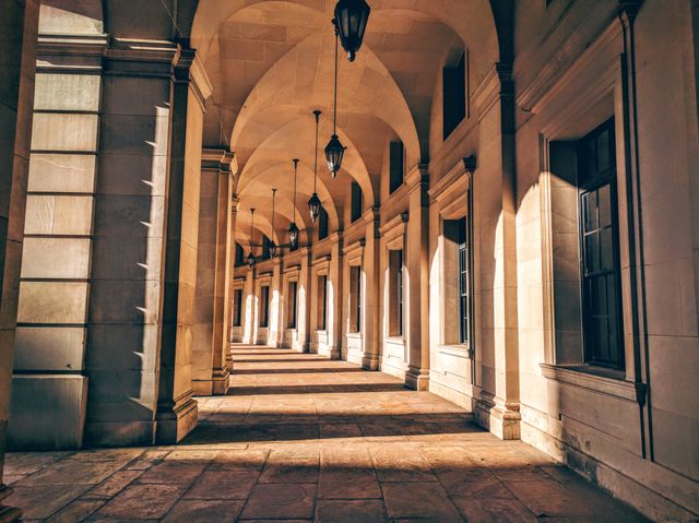 This is a corridor surrounded by a series of arches with sunlight piercing through, creating shadows. The stone pathway and symmetrical arches convey a sense of historical significance and timeless elegance. This image is perfect for use in projects related to history, architecture, travel, or to evoke feelings of tranquility and peace.