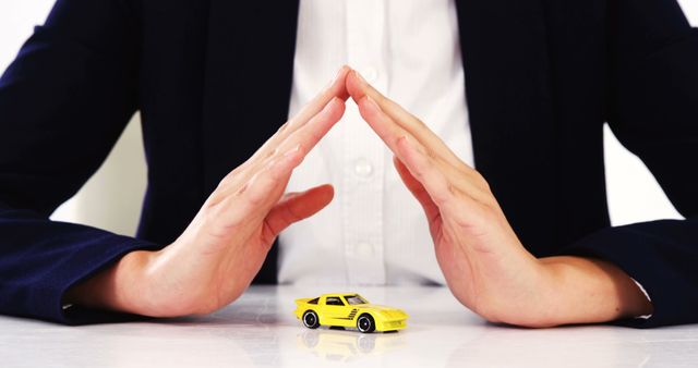 Hands of caucasian businesswoman sheltering yellow car with copy space. Transport, travel, business, finance and technology concept, unaltered.