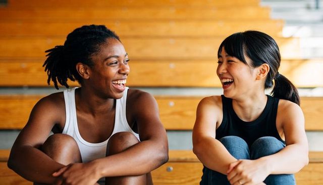 Laughing friends resting on wooden gym bleachers during casual workout break