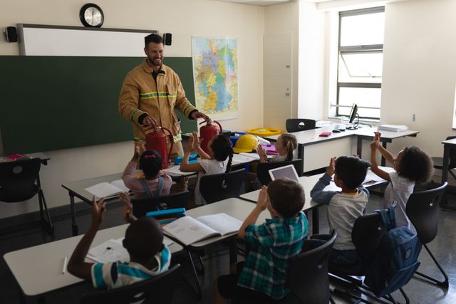 Firefighter teaching fire safety to elementary school children in a classroom. Children are sitting at desks, applauding and engaging with the firefighter. Ideal for educational materials, safety training programs, school brochures, and community safety campaigns.