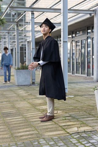 Asian graduate celebrating under pergola at modern university courtyard in cap and gown
