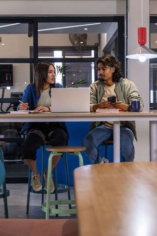 Diverse coworkers collaborating and brainstorming at high table in coworking space with laptop