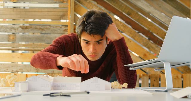 This captures an architecture student concentrating on a model house. Ideal for blogs about education in architecture, promoting creative spaces, and academic websites. Can be used in promotional materials highlighting architectural education and career development in design fields.