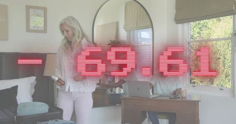 Couple juggling remote work and packing with red -69.61 overlay in bedroom with mirror