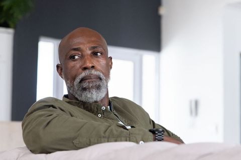 Thoughtful african american senior man relaxing on sofa in minimalist living room