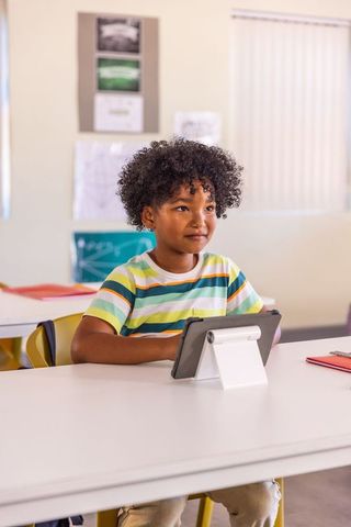 Curly-haired african american child using tablet in classroom for focused digital learning
