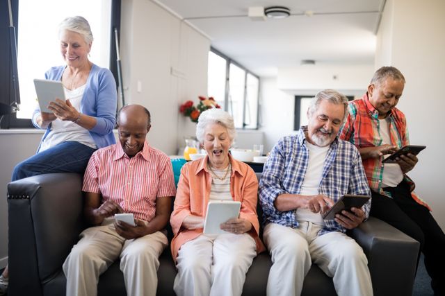 Smiling senior people using tablet computer while sitting on couch at nursing home