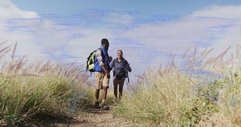 Two hikers hiking coastal hillside trail with backpacks and trekking poles under blue sky