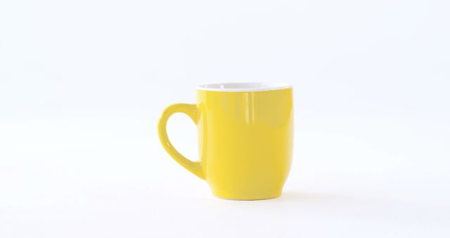 A vibrant yellow mug stands out against a clean white background, with copy space. Its bright color adds a cheerful touch to the minimalist setting, ideal for a morning coffee or tea.